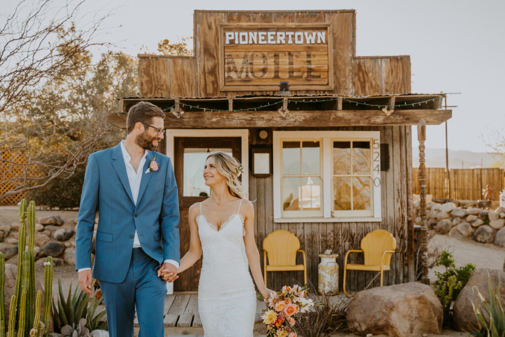 Pioneertown couple in their wedding outfits posing in front of the Pioneertown Motel office.